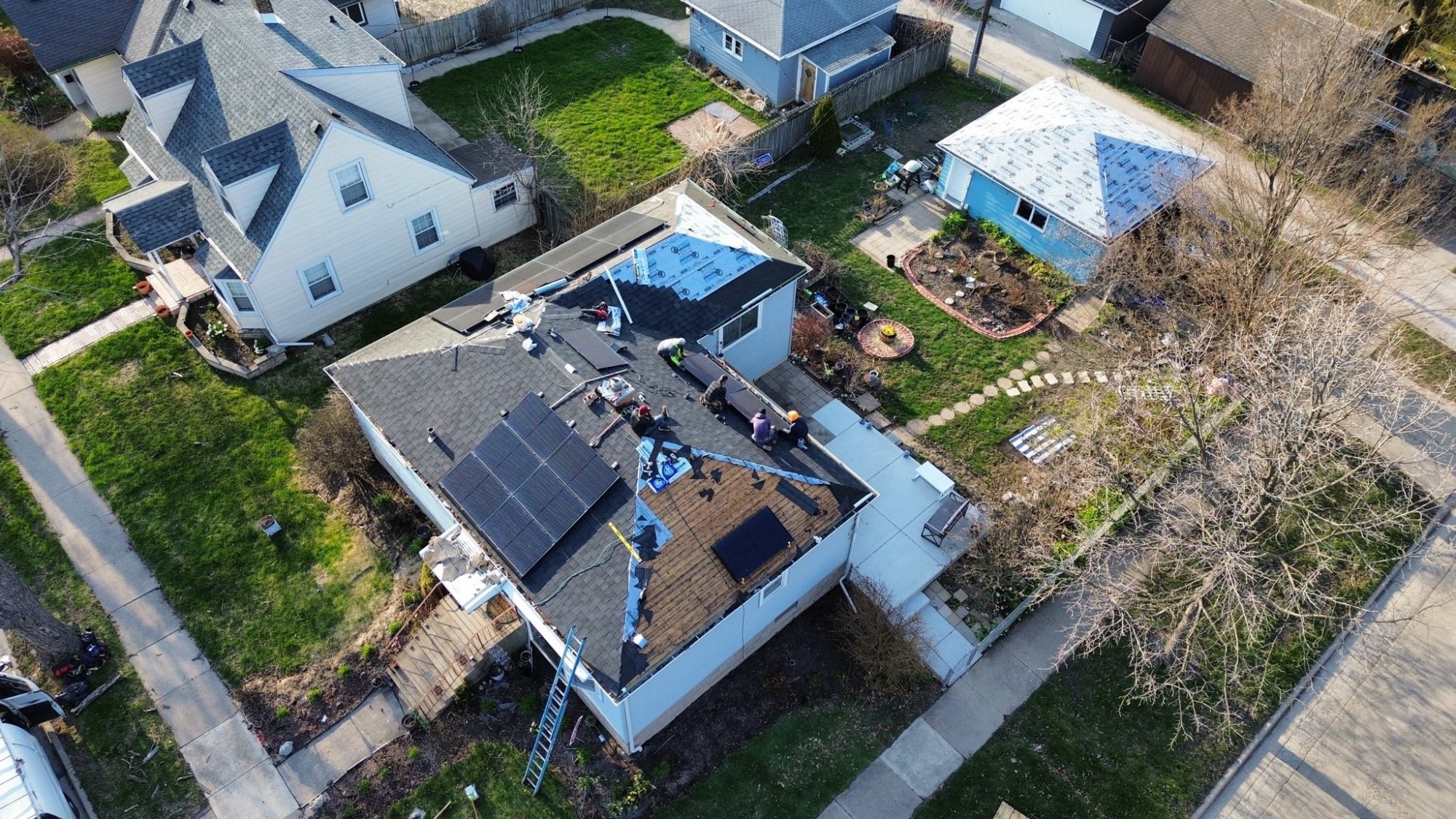 Drone view of roofing crew installing shingles with solar panels