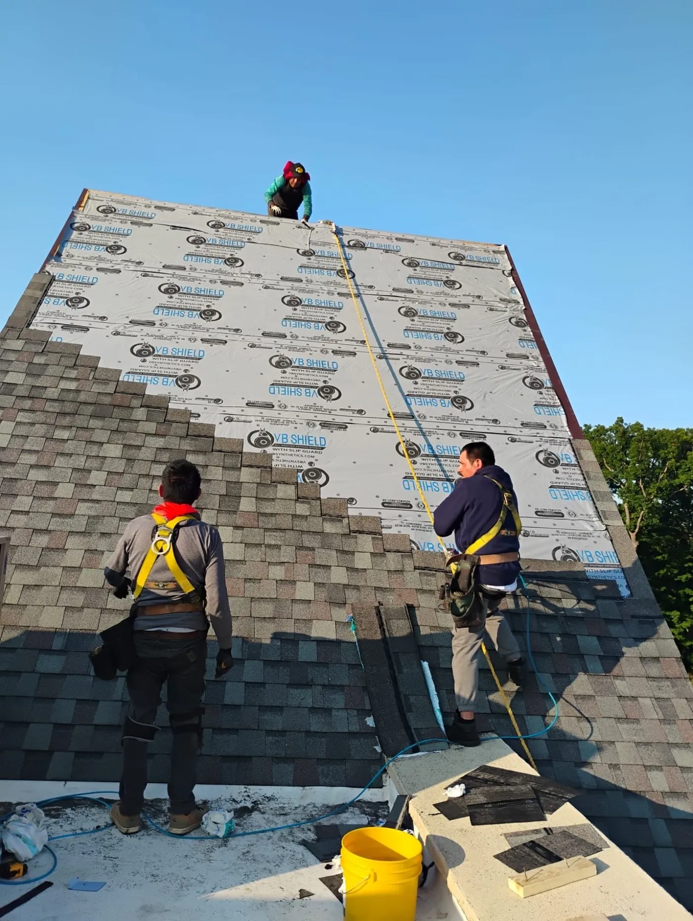 Roofing crew installing shingles on steep pitch roof