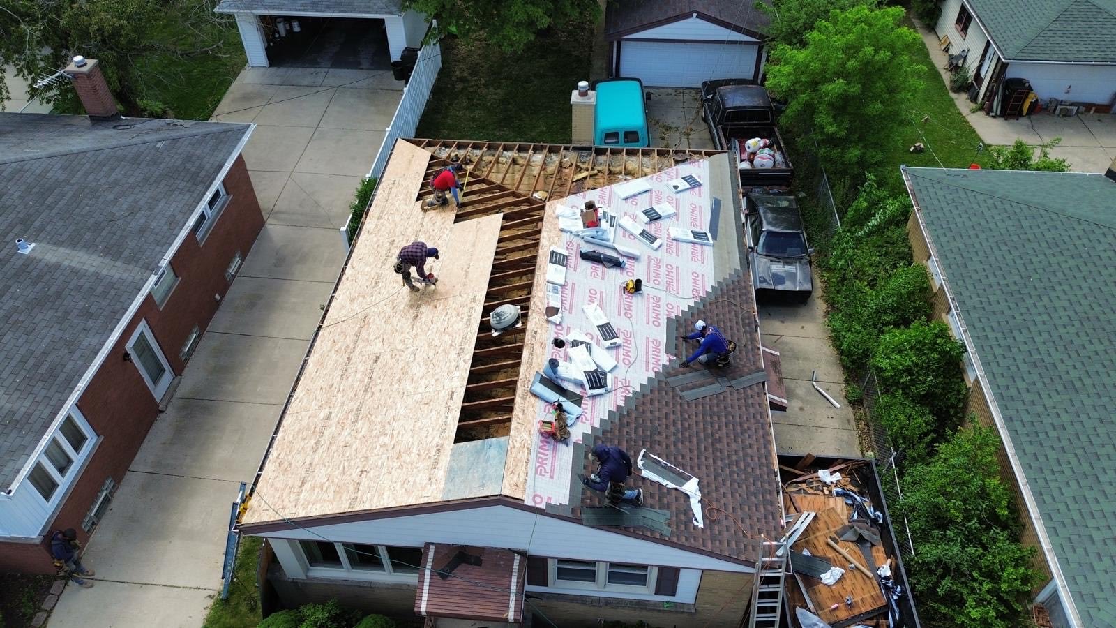 Aerial drone shot of crew mid-replacement — plywood decking and underlayment being installed