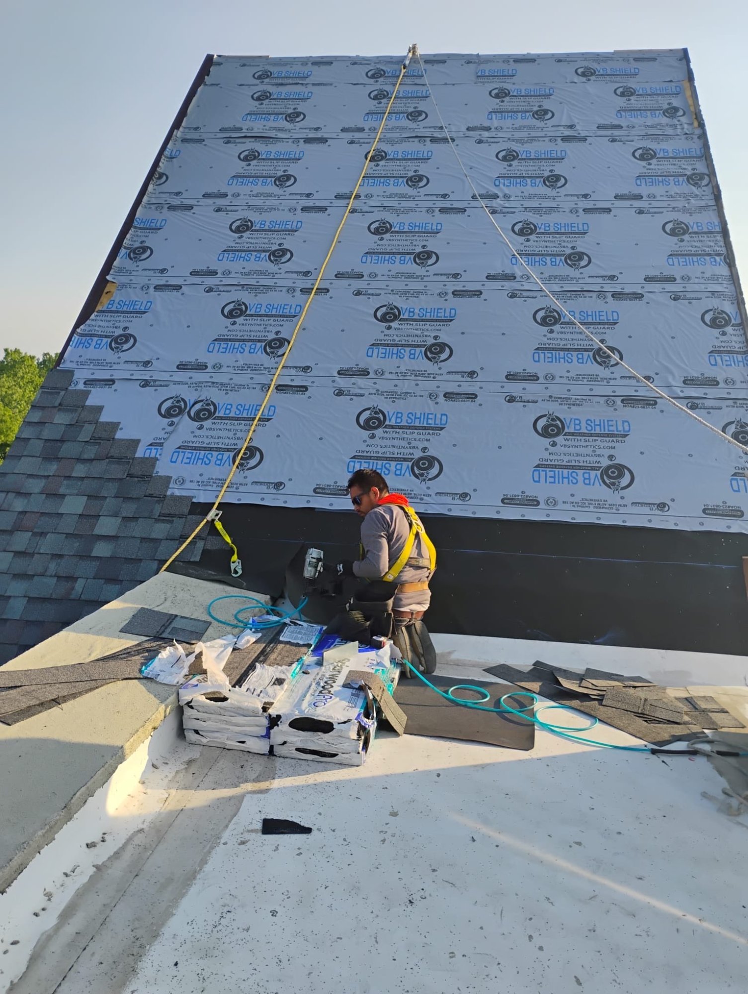 Worker in safety harness installing VB Shield underlayment on steep residential roof